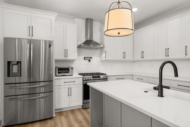 kitchen with decorative light fixtures, wall chimney exhaust hood, stainless steel appliances, and white cabinetry