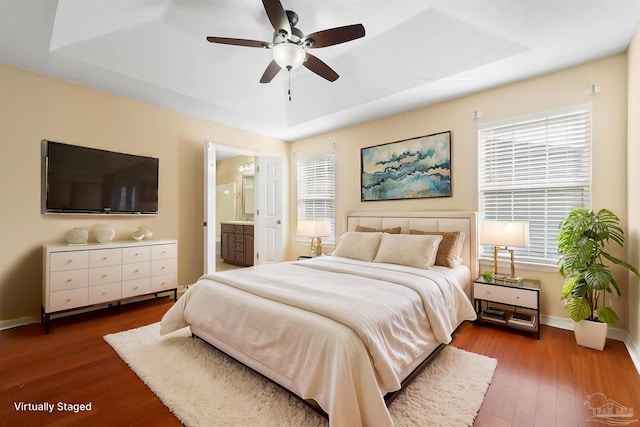 bedroom featuring ceiling fan, ensuite bathroom, dark hardwood / wood-style flooring, and a raised ceiling