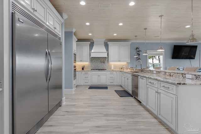 kitchen with tasteful backsplash, stainless steel appliances, light stone counters, premium range hood, and sink