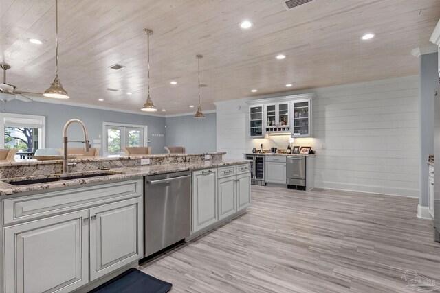 kitchen featuring hanging light fixtures, sink, stainless steel dishwasher, light hardwood / wood-style floors, and light stone counters