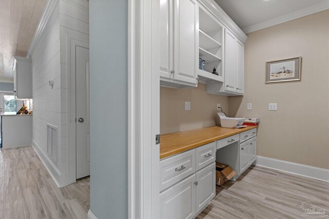 kitchen with white cabinets, light wood-type flooring, ornamental molding, and built in desk