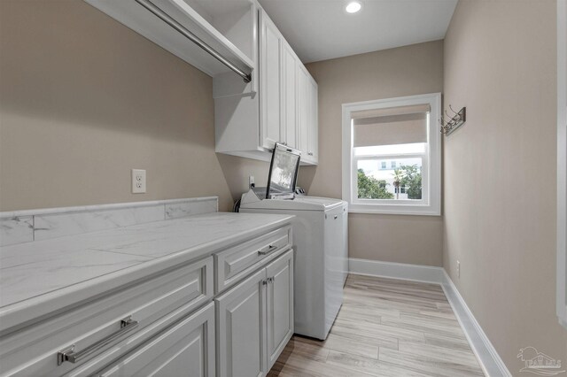 laundry area featuring washing machine and clothes dryer, light hardwood / wood-style flooring, and cabinets