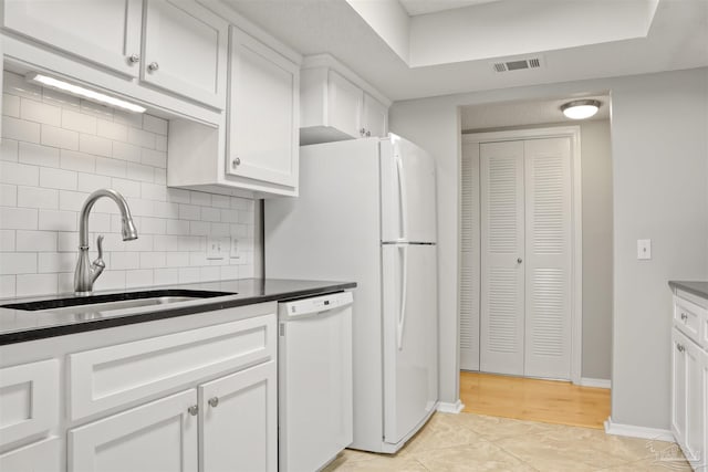 kitchen featuring white dishwasher, a sink, visible vents, white cabinets, and decorative backsplash