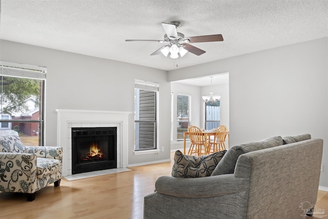 living room with baseboards, a tile fireplace, wood finished floors, a textured ceiling, and ceiling fan with notable chandelier