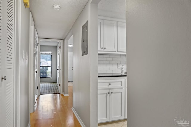 corridor with baseboards, electric panel, and light wood-style floors