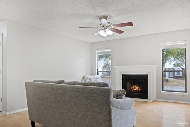 living room featuring a fireplace with flush hearth, ceiling fan, light wood-style flooring, and baseboards