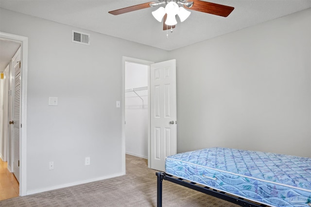 bedroom featuring a walk in closet, a closet, visible vents, light carpet, and baseboards