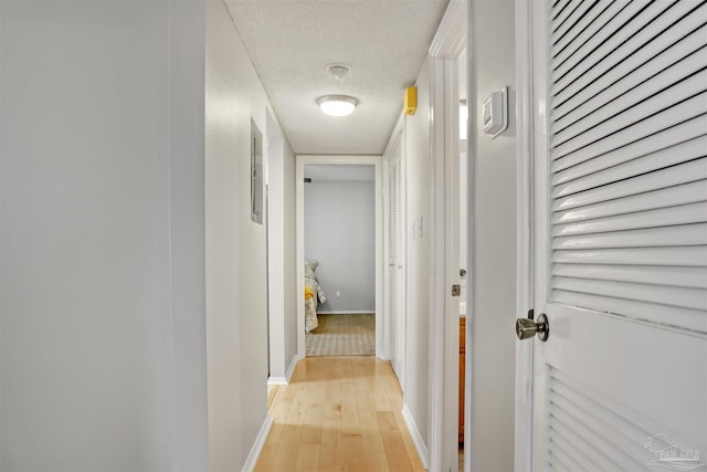 hall featuring light wood-style floors, baseboards, and a textured ceiling