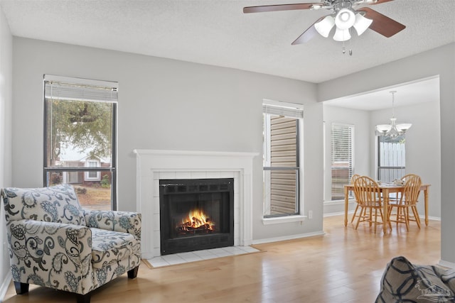 living area featuring a textured ceiling, baseboards, wood finished floors, and a tile fireplace