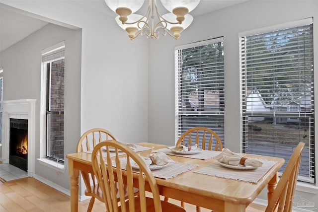 dining space featuring a fireplace with flush hearth, a notable chandelier, light wood-style flooring, and baseboards