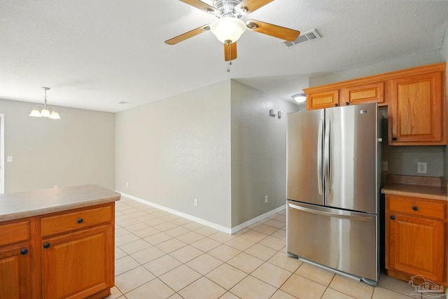 kitchen with visible vents, brown cabinets, light countertops, freestanding refrigerator, and ceiling fan with notable chandelier