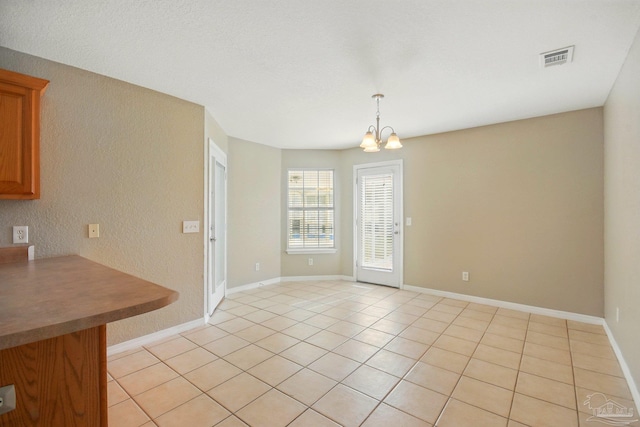 interior space with an inviting chandelier, visible vents, a textured wall, light tile patterned flooring, and baseboards