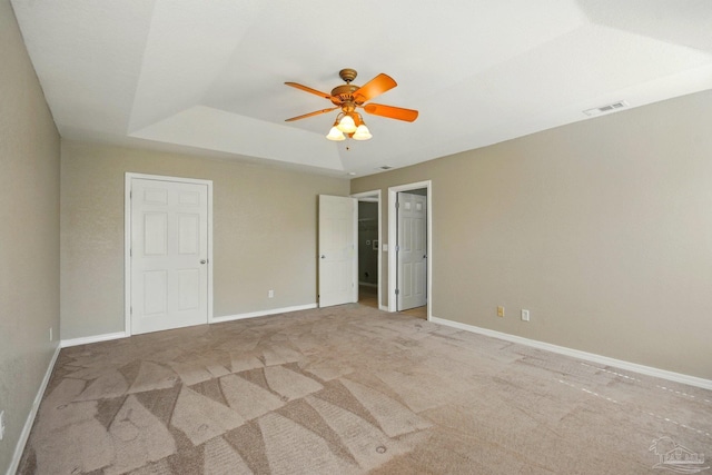 carpeted spare room with a ceiling fan, a tray ceiling, visible vents, and baseboards
