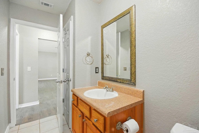 bathroom featuring visible vents, tile patterned flooring, vanity, baseboards, and a textured wall
