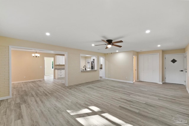 unfurnished living room featuring sink, ceiling fan with notable chandelier, and light wood-type flooring