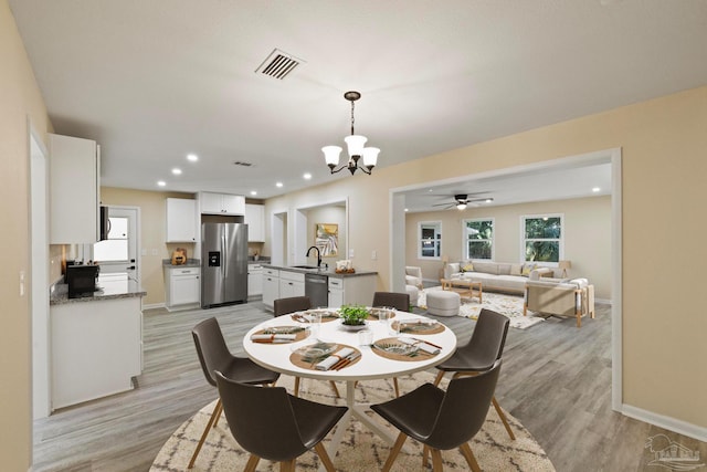 dining room with ceiling fan with notable chandelier, sink, and light hardwood / wood-style flooring