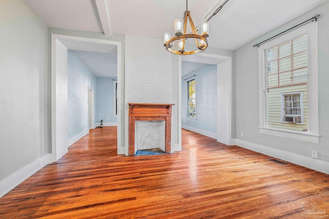 unfurnished living room with hardwood / wood-style flooring, a healthy amount of sunlight, an inviting chandelier, and a fireplace