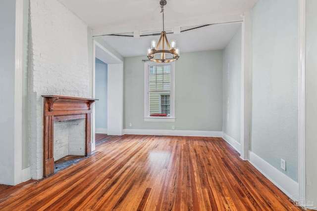 unfurnished dining area with a notable chandelier, a stone fireplace, and wood-type flooring