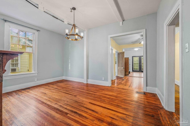 unfurnished dining area with wood-type flooring, ceiling fan with notable chandelier, and beam ceiling