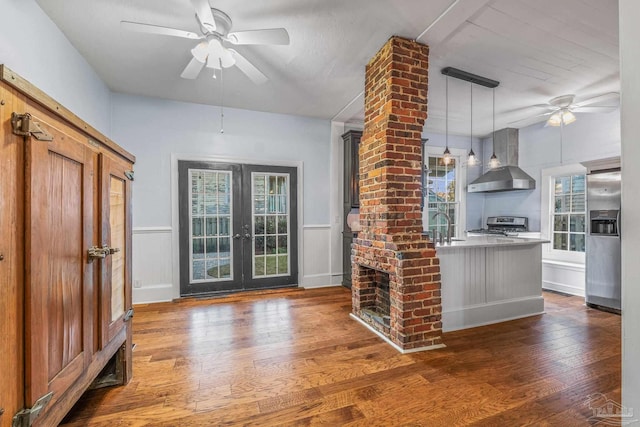 kitchen with dark wood-type flooring, stainless steel appliances, decorative light fixtures, and wall chimney range hood