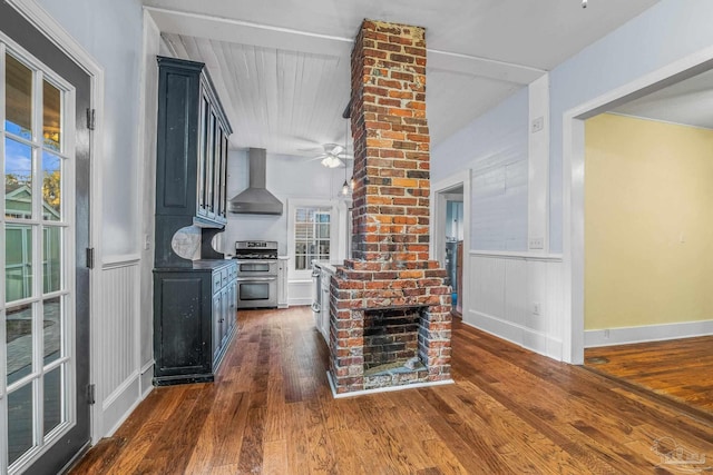 kitchen with wall chimney exhaust hood, dark hardwood / wood-style flooring, ceiling fan, a fireplace, and range with two ovens