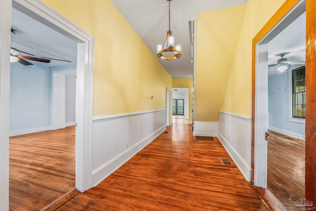 hallway with hardwood / wood-style flooring, lofted ceiling, and a notable chandelier