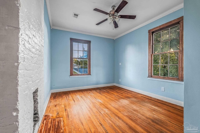 empty room featuring hardwood / wood-style floors, crown molding, a stone fireplace, and ceiling fan