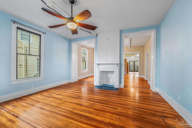 unfurnished living room with ceiling fan, a large fireplace, and light hardwood / wood-style floors