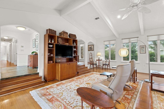 living area featuring arched walkways, a textured ceiling, vaulted ceiling with beams, visible vents, and hardwood / wood-style floors