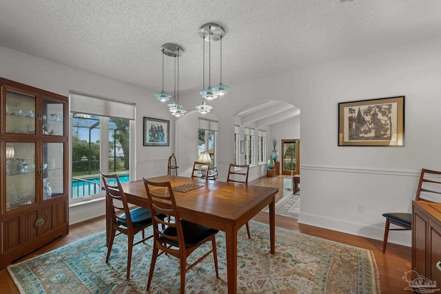 dining room featuring arched walkways, a textured ceiling, lofted ceiling, wood finished floors, and baseboards