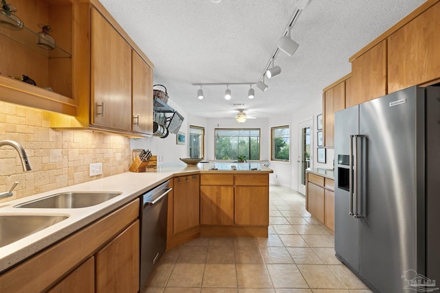 kitchen featuring brown cabinetry, appliances with stainless steel finishes, a peninsula, light countertops, and light tile patterned flooring