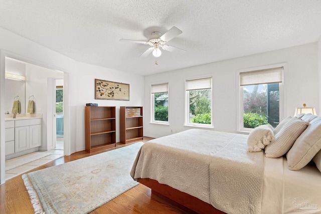 bedroom with light wood-type flooring, ceiling fan, connected bathroom, and a textured ceiling