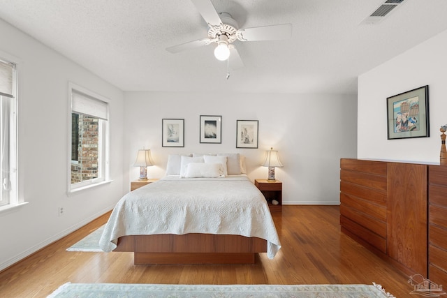 bedroom featuring a textured ceiling, wood finished floors, visible vents, and baseboards