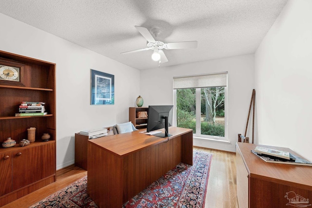 home office featuring a ceiling fan, baseboards, a textured ceiling, and light wood finished floors