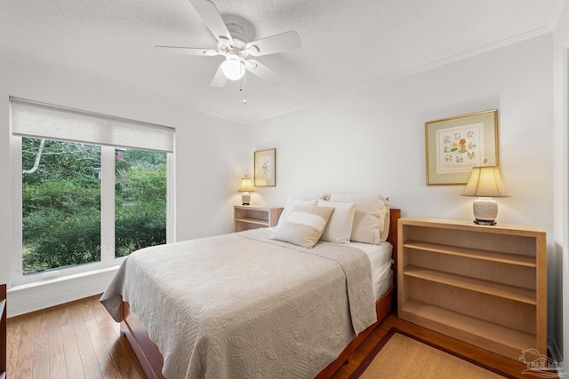 bedroom featuring a ceiling fan, wood-type flooring, multiple windows, and ornamental molding