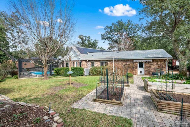 rear view of house featuring glass enclosure, brick siding, a garden, a yard, and a fenced in pool