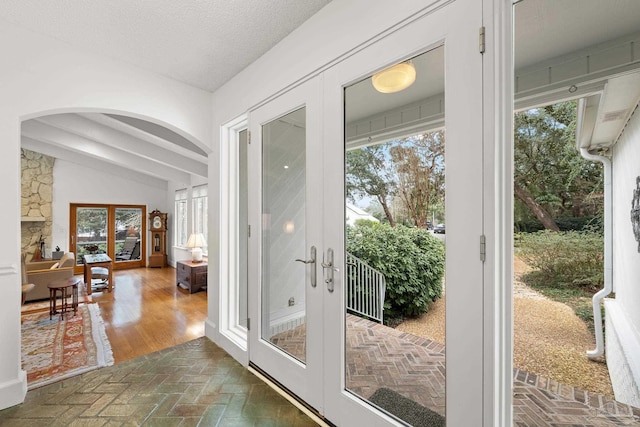 doorway featuring arched walkways, brick floor, vaulted ceiling, a textured ceiling, and french doors