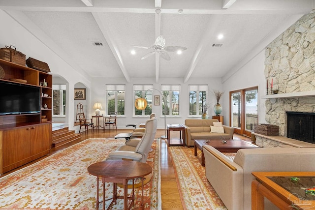 living room featuring visible vents, vaulted ceiling with beams, a textured ceiling, light wood-type flooring, and a fireplace