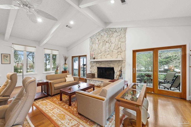 living area with vaulted ceiling with beams, light wood-style floors, a ceiling fan, and a stone fireplace