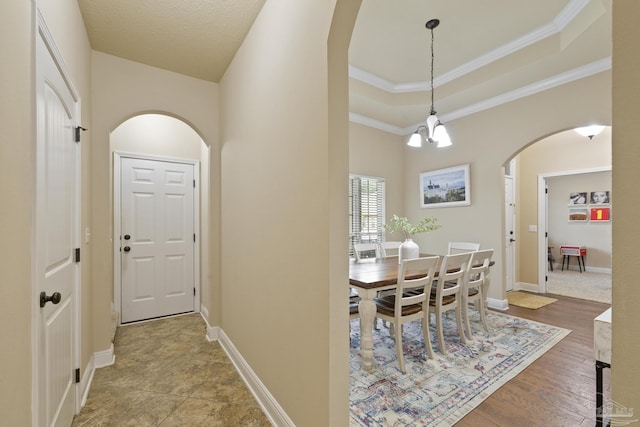 corridor with arched walkways, a tray ceiling, a chandelier, and baseboards