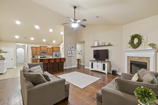 living area with arched walkways, a tile fireplace, visible vents, baseboards, and dark wood finished floors