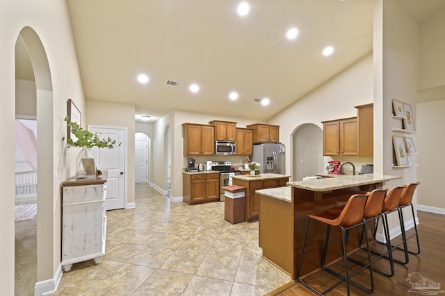 kitchen with arched walkways, brown cabinets, appliances with stainless steel finishes, a peninsula, and a kitchen breakfast bar