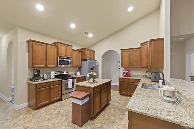 kitchen featuring arched walkways, stainless steel appliances, a peninsula, a sink, and brown cabinetry