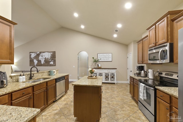 kitchen featuring arched walkways, a center island, light stone countertops, stainless steel appliances, and a sink