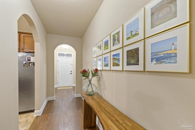 doorway featuring arched walkways, a textured ceiling, baseboards, and wood finished floors