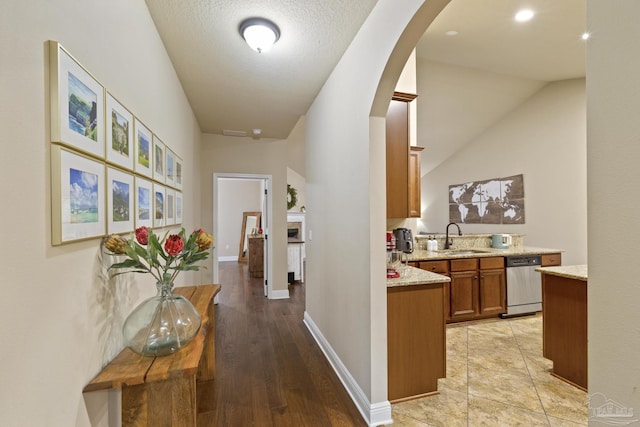 corridor with arched walkways, a textured ceiling, a sink, and baseboards