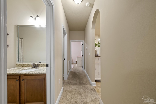 corridor featuring arched walkways, baseboards, a sink, and light colored carpet