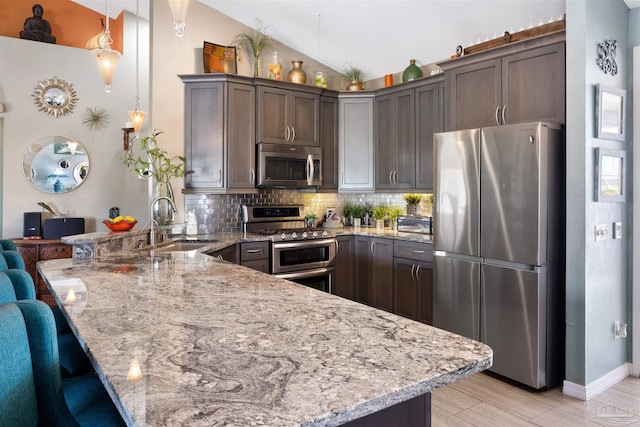 kitchen featuring a sink, light stone countertops, tasteful backsplash, appliances with stainless steel finishes, and a peninsula