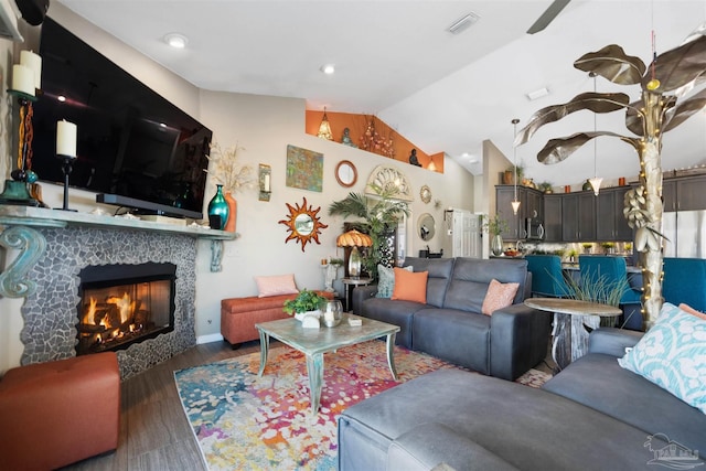 living room featuring a tiled fireplace, ceiling fan, vaulted ceiling, and wood finished floors