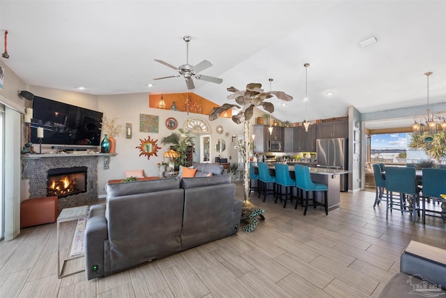 living room with a tiled fireplace, light wood-style flooring, ceiling fan with notable chandelier, and lofted ceiling